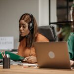 Two call center agents collaborating with laptops in a modern office.